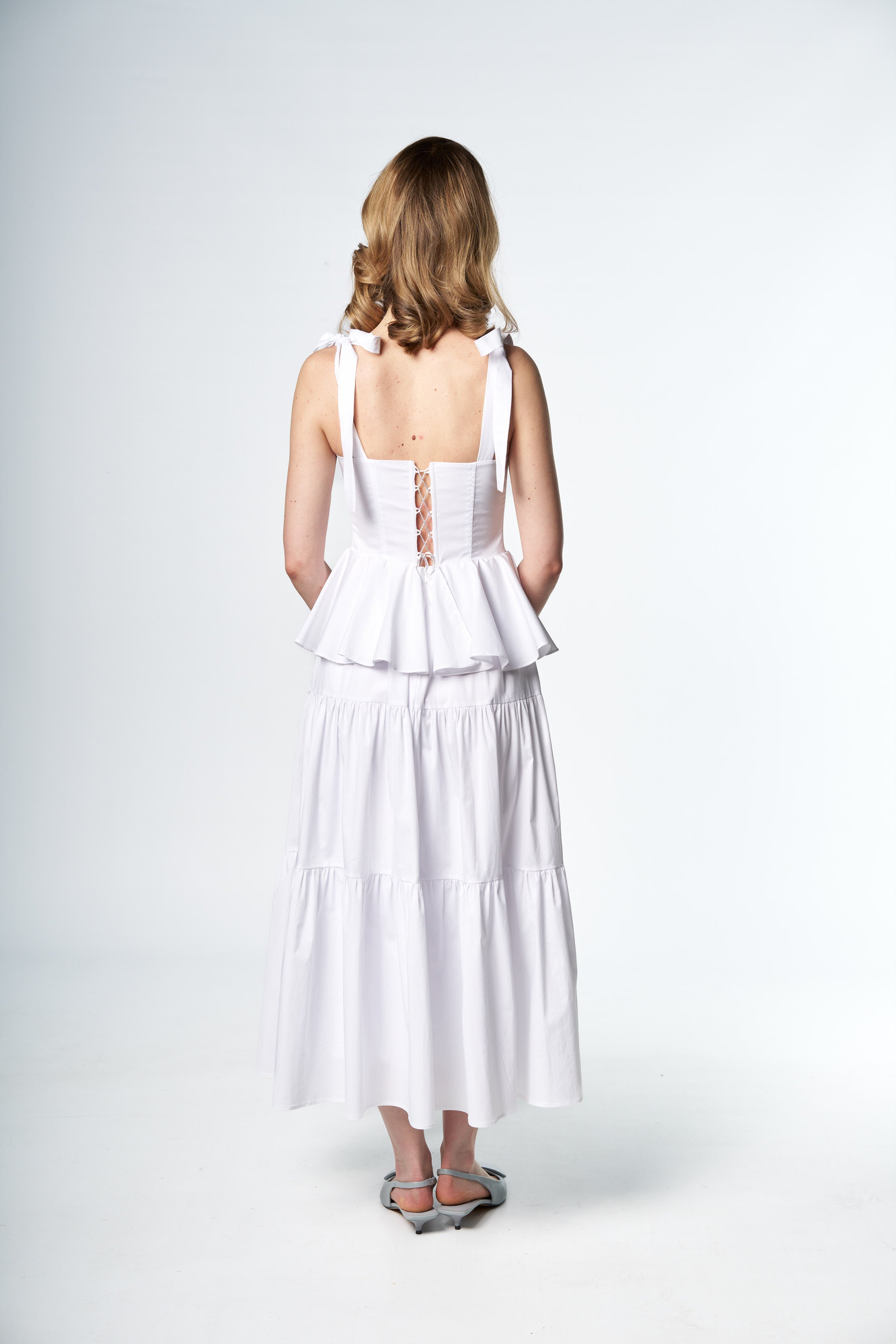 Woman wearing a white dress with a cut-out back design on a white background